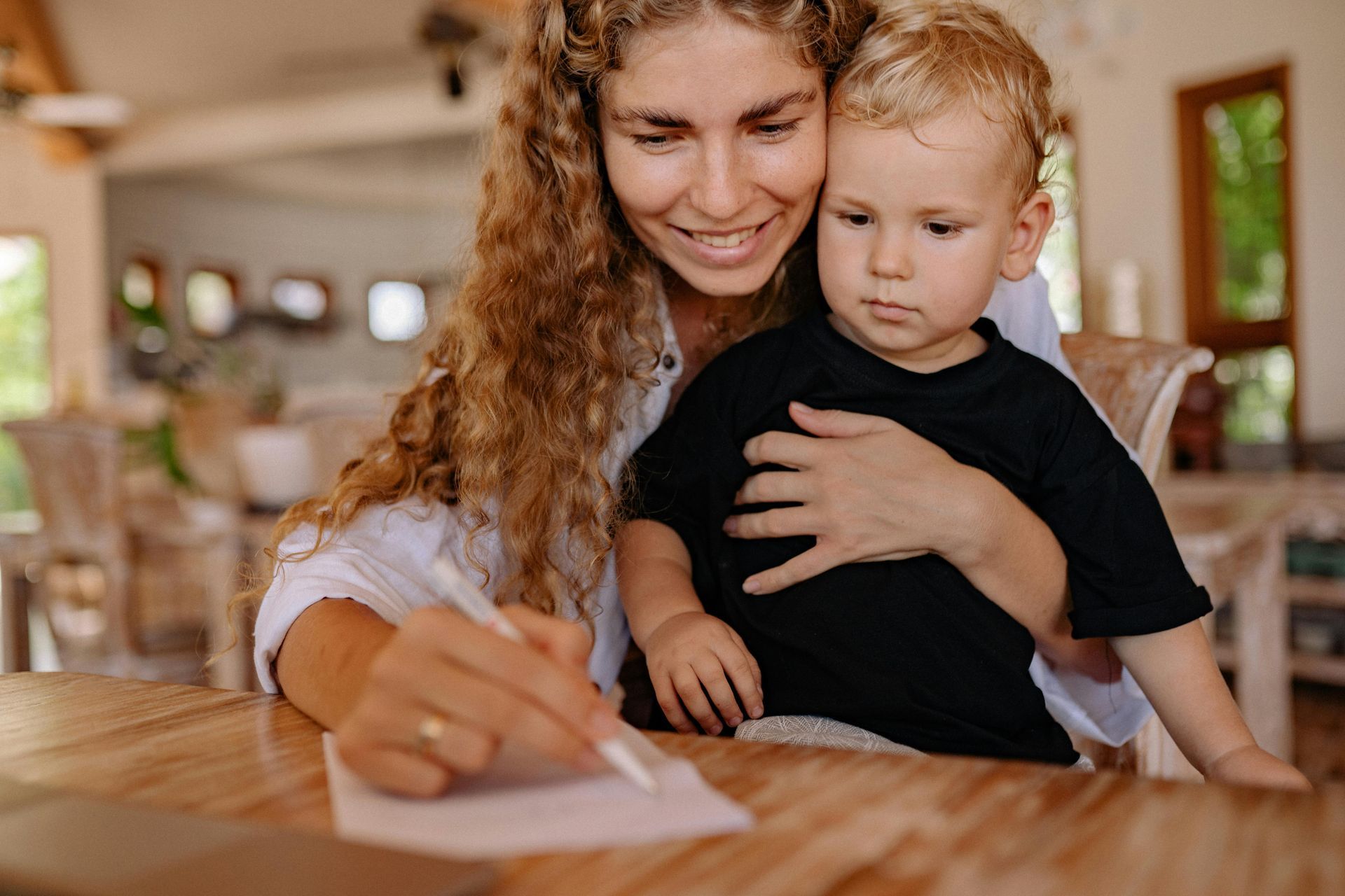 Woman and toddler writing together at a wooden table in a bright home interior