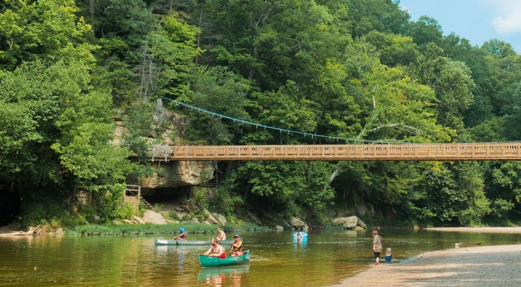 Canoes on a calm river beside a wooden bridge and lush green forest.