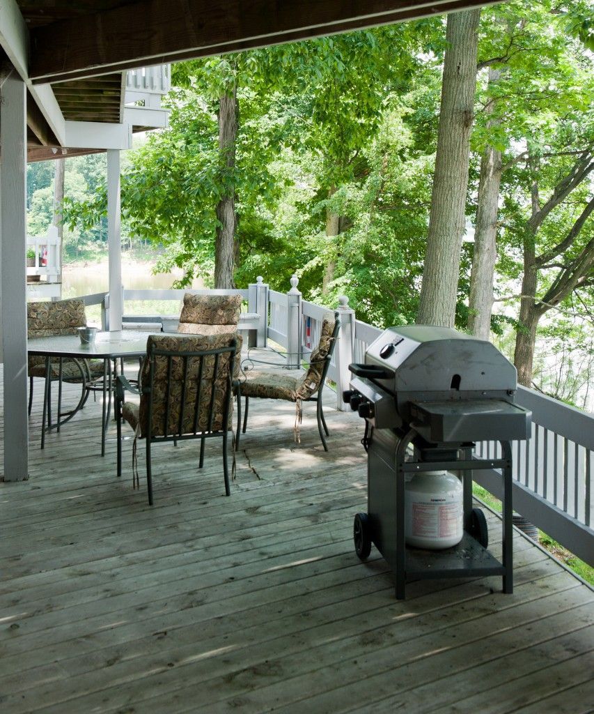 Covered wooden deck with patio table, chairs, and a gas grill overlooking green trees