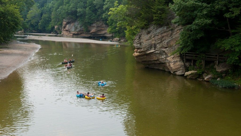 River canyon with kayakers paddling in calm green water between rocky, tree-lined banks