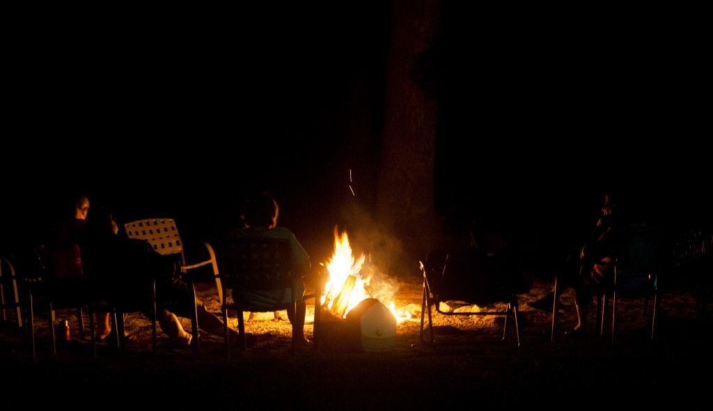 People seated around a campfire at night in a dark outdoor setting