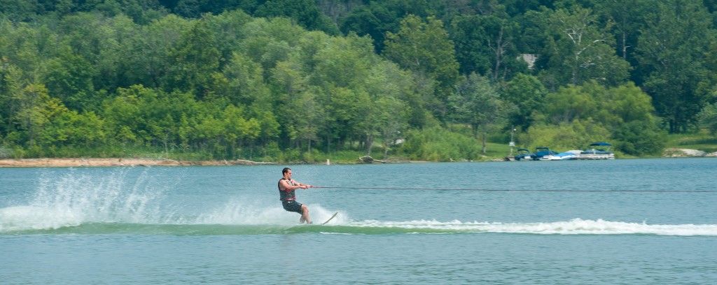 Wakeboarder skimming across a lake with a forested shoreline in the background