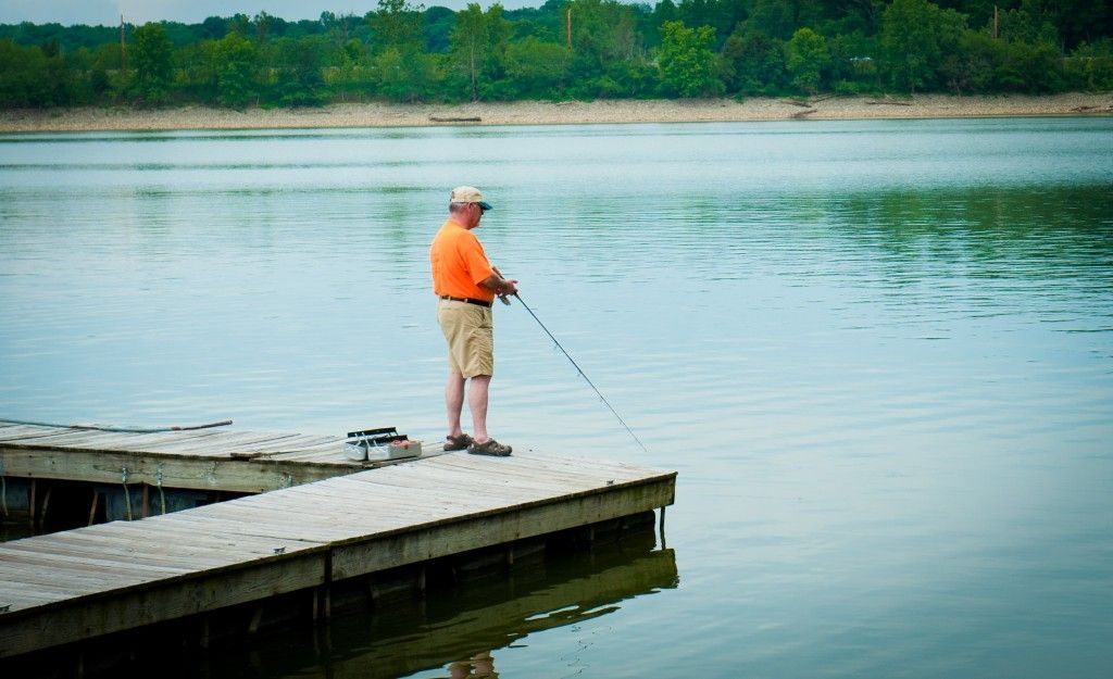 Person in an orange shirt fishing from a wooden dock on a calm lake