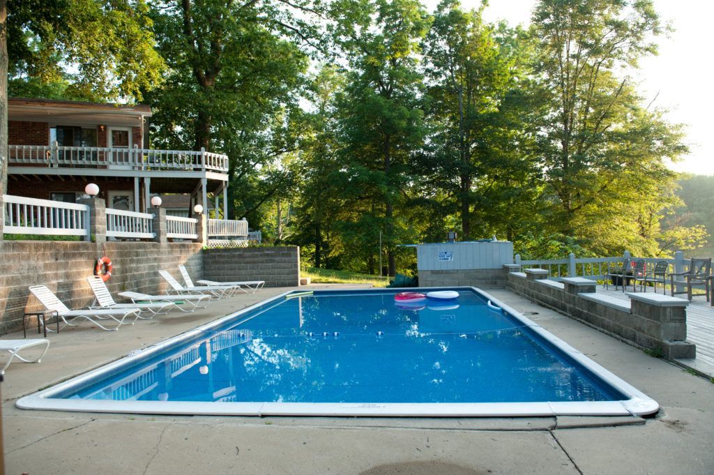 Outdoor swimming pool beside a house, with a blue cover and trees in the background