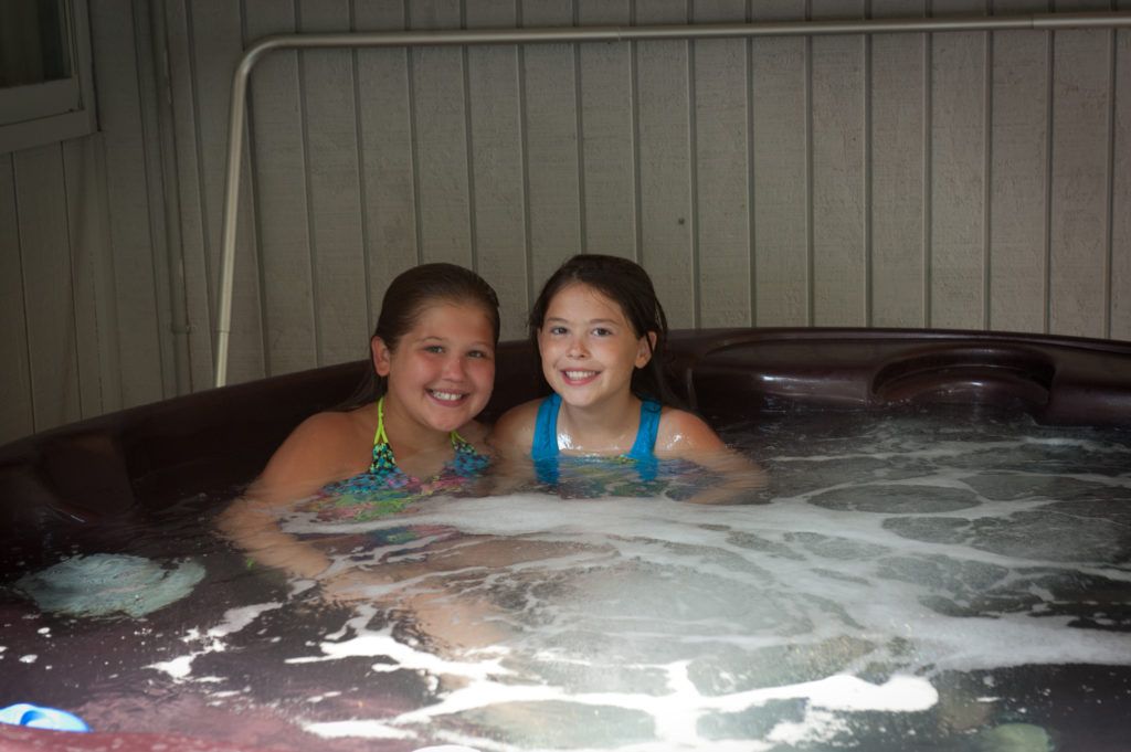 Two children smiling in a bubbling hot tub indoors