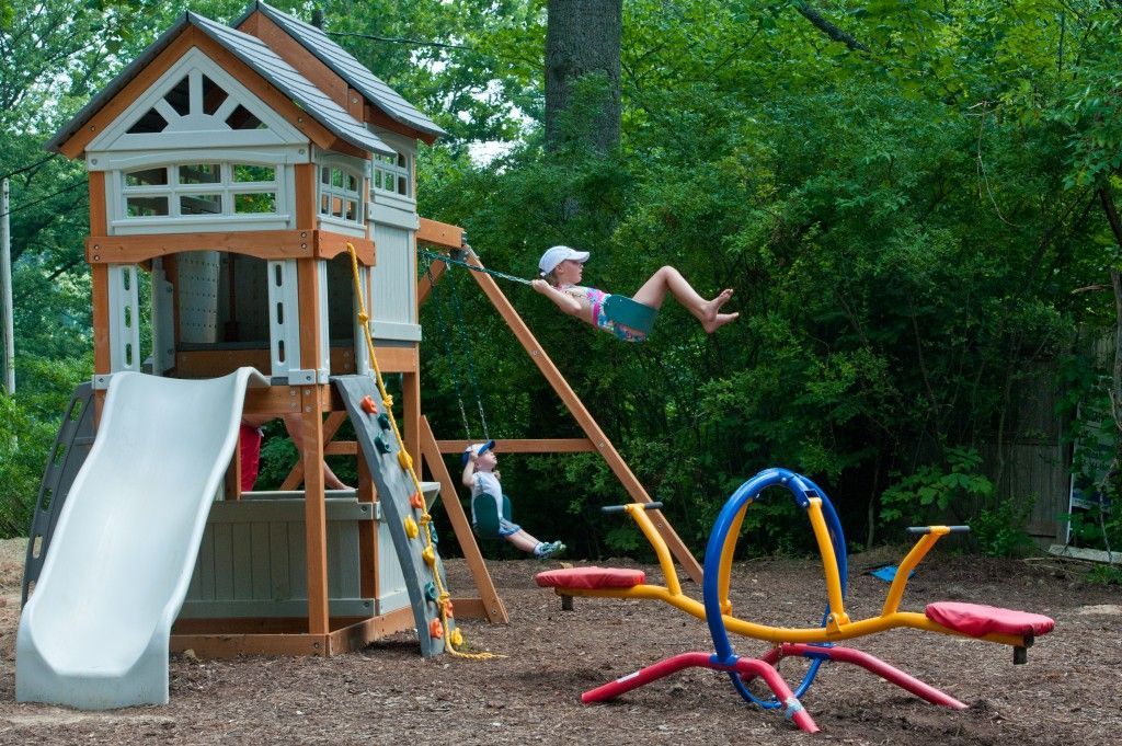 Backyard playground with slide, swings, and a child swinging on a rope swing