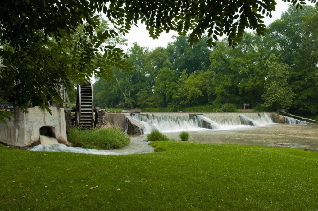 Small waterfall beside a green lawn and trees, with a staircase on the left.