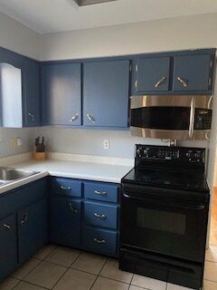 Blue kitchen with black stove and microwave, white countertops, and tiled floor.