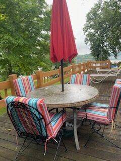 Outdoor patio table with colorful striped chairs and a closed red umbrella overlooking trees and water