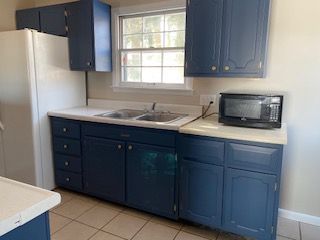 Kitchen with dark blue cabinets, white countertop, sink under window, and a microwave on the counter.