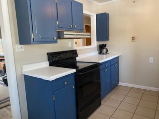 Small kitchen with blue cabinets, black stove, white countertops, and beige tile floor.