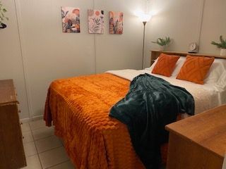 Cozy bedroom with orange bedspread, teal throw, floor lamp, and wall art.