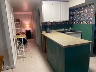 Small kitchen with green island, white cabinets, floral backsplash, and a narrow hallway beyond.
