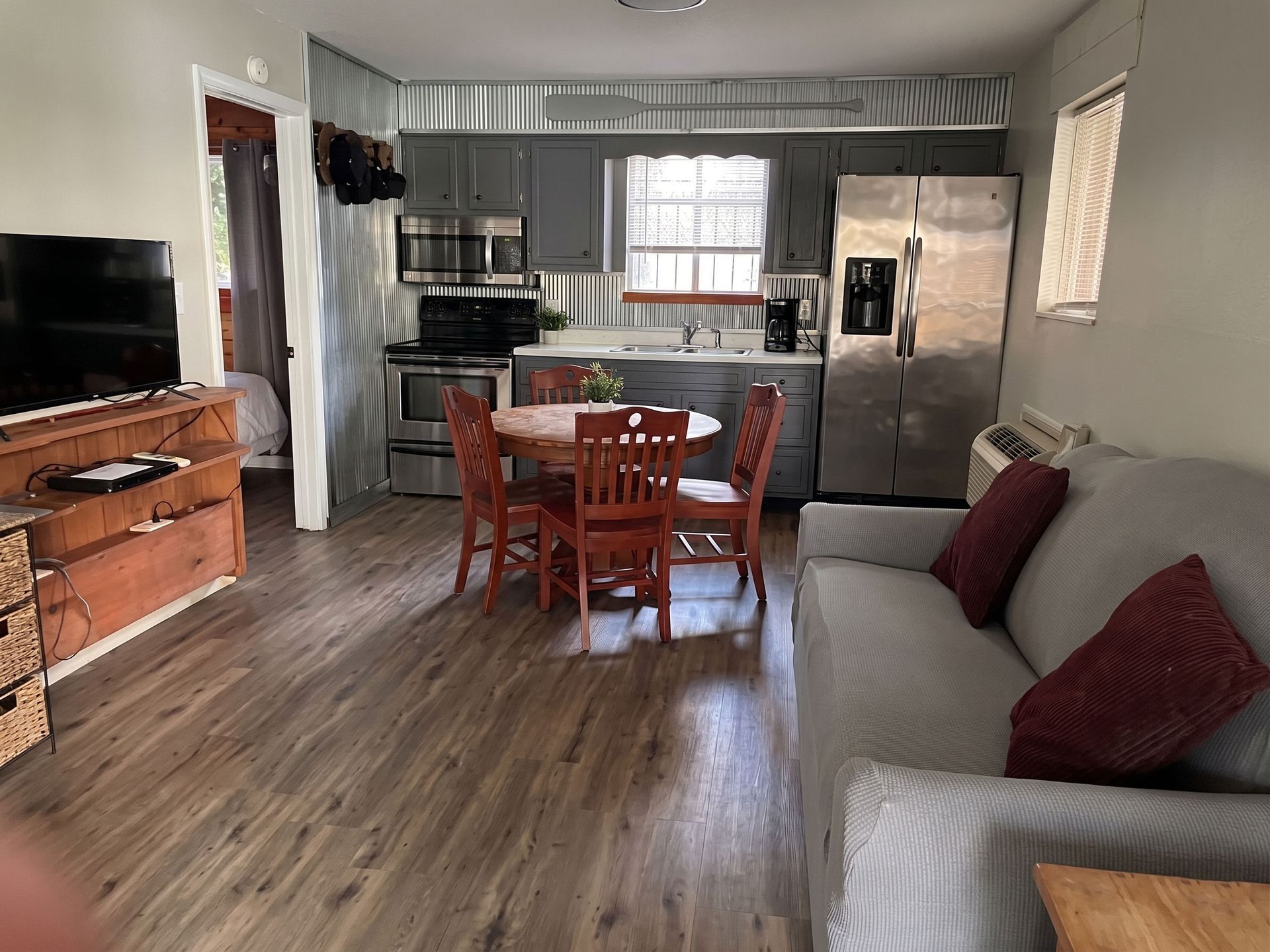 Open living room and kitchen with gray sofa, wooden table, stainless fridge, and wood flooring