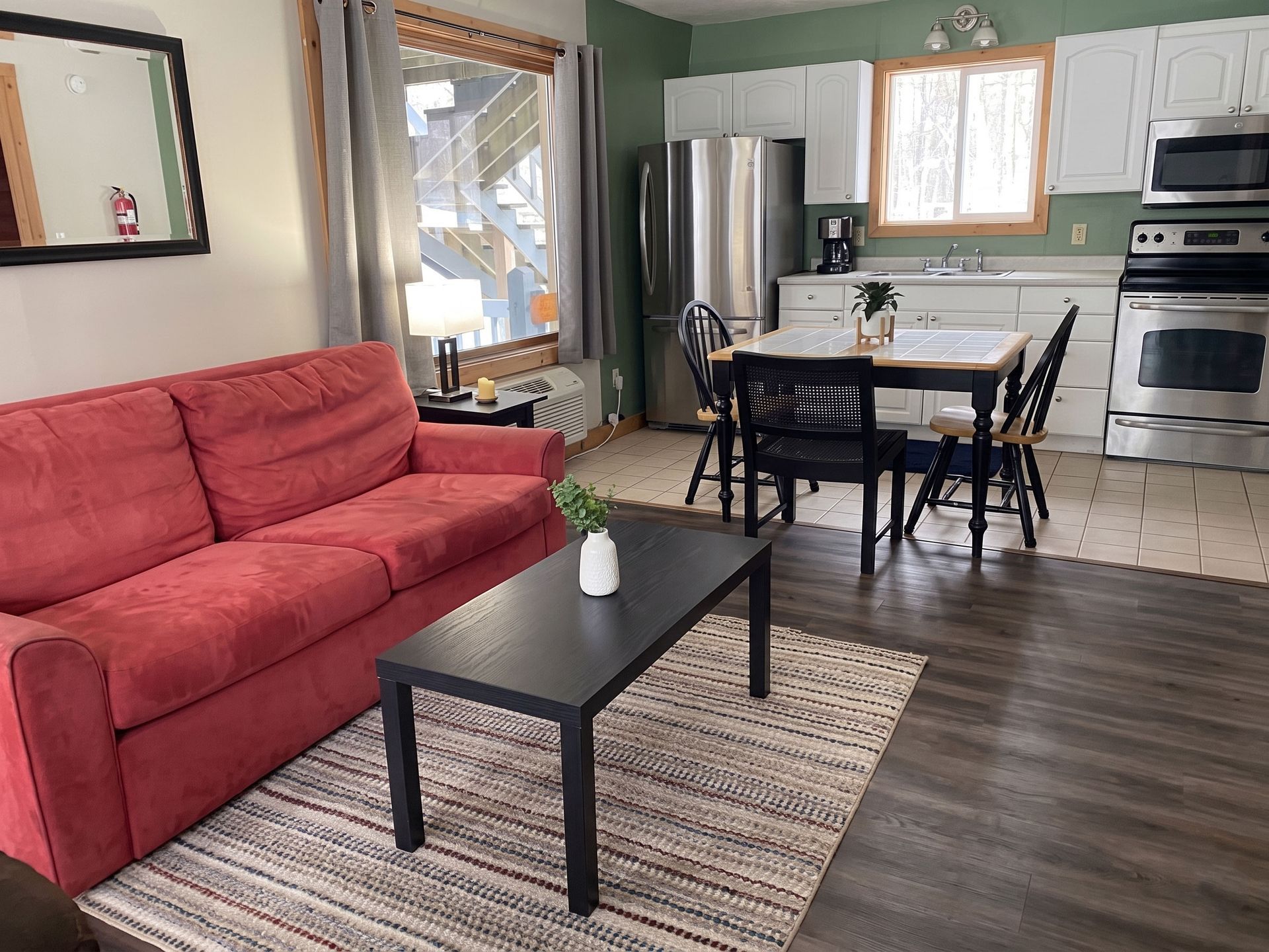 Small apartment living room and kitchen with a red sofa, coffee table, dining set, and stainless steel appliances.