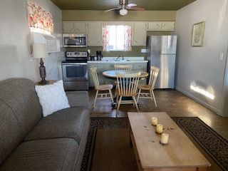 Small living room with gray sofa, coffee table, dining set, and kitchen in the background