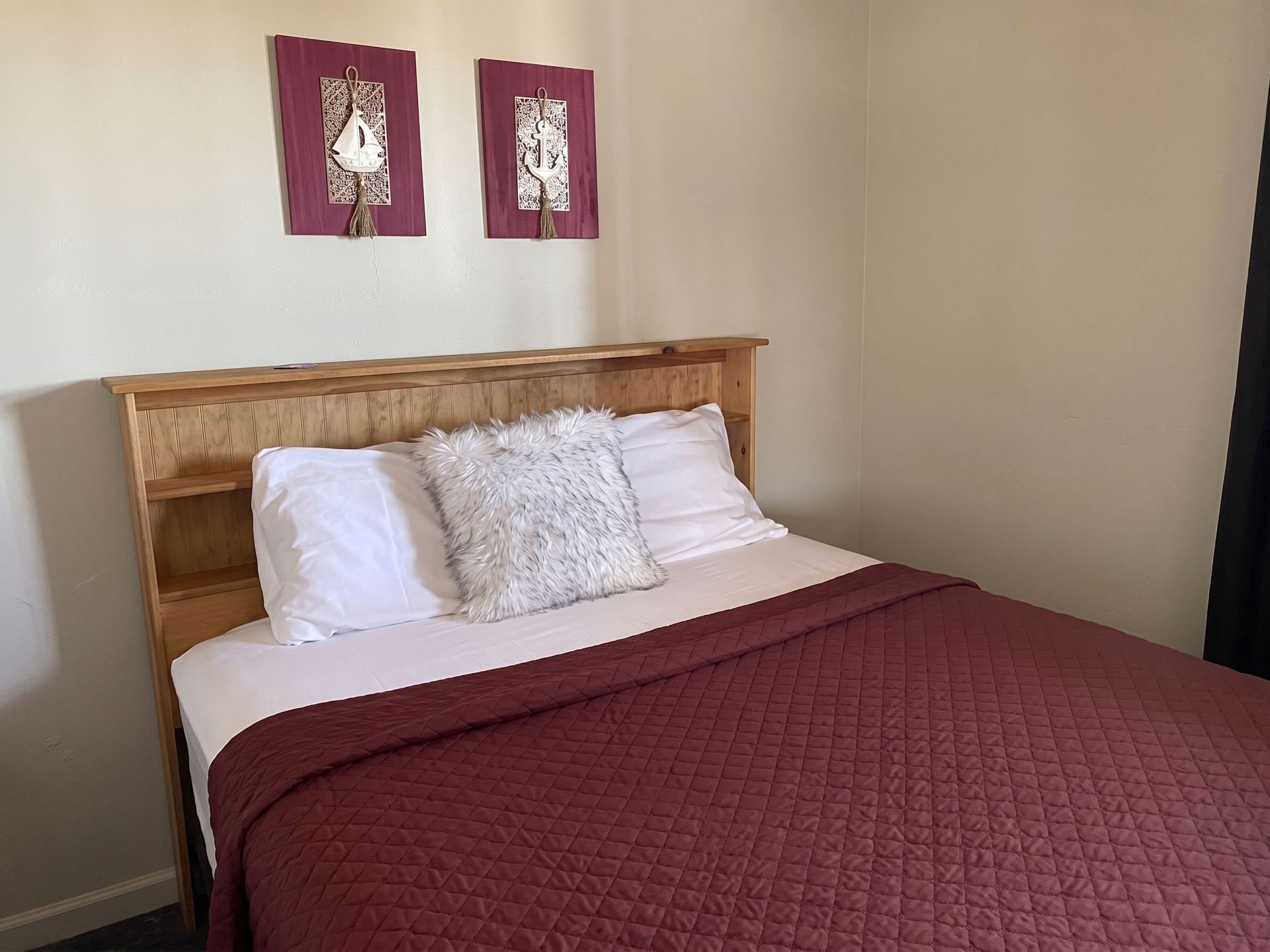 Bedroom with wooden headboard, burgundy quilt, white pillows, and two framed wall prints