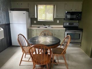 Small kitchen with white cabinets, stove, fridge, sink, and round table with wooden chairs.