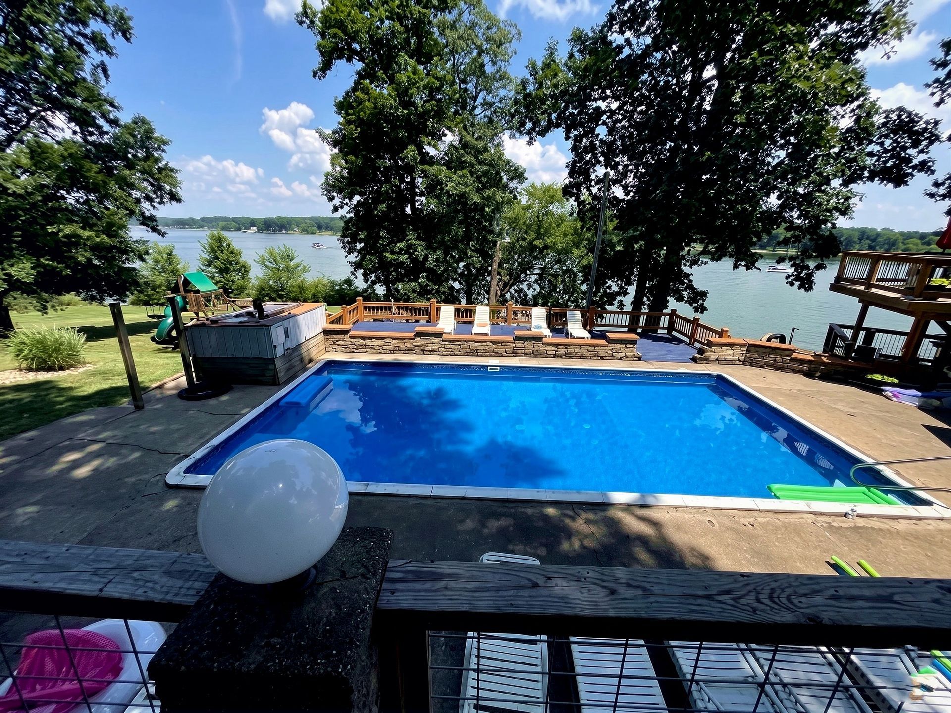 Backyard pool with lounge chairs, trees, and a lake view on a sunny day