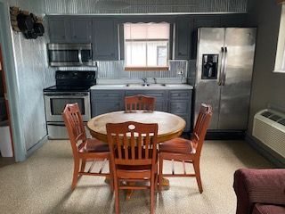 Small kitchen with stainless appliances and a round wooden table surrounded by four chairs.