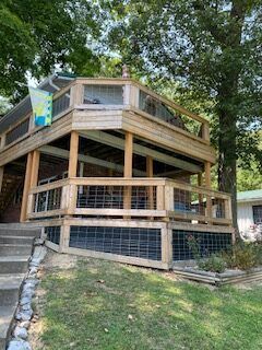 Wooden multi-level deck or treehouse on a sloped yard with railings and trees overhead