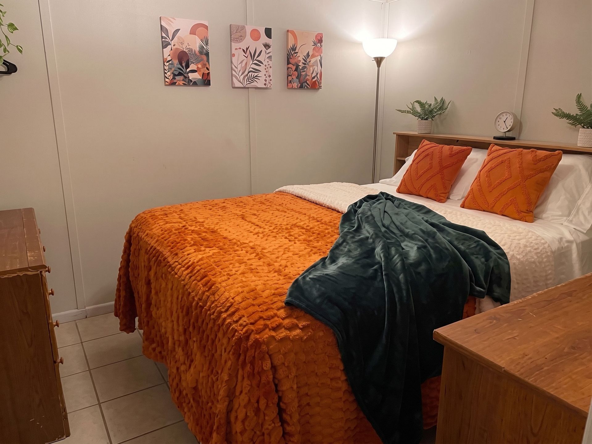 Cozy bedroom with orange bedding, teal throw, wall art, and a floor lamp.