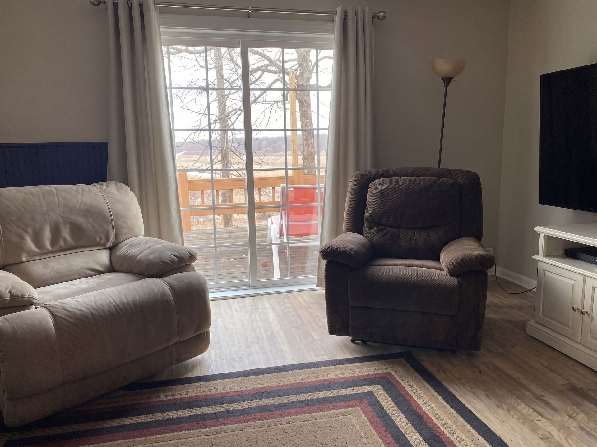 Living room with sofa, recliner, TV, floor lamp, and sliding glass door to a balcony.