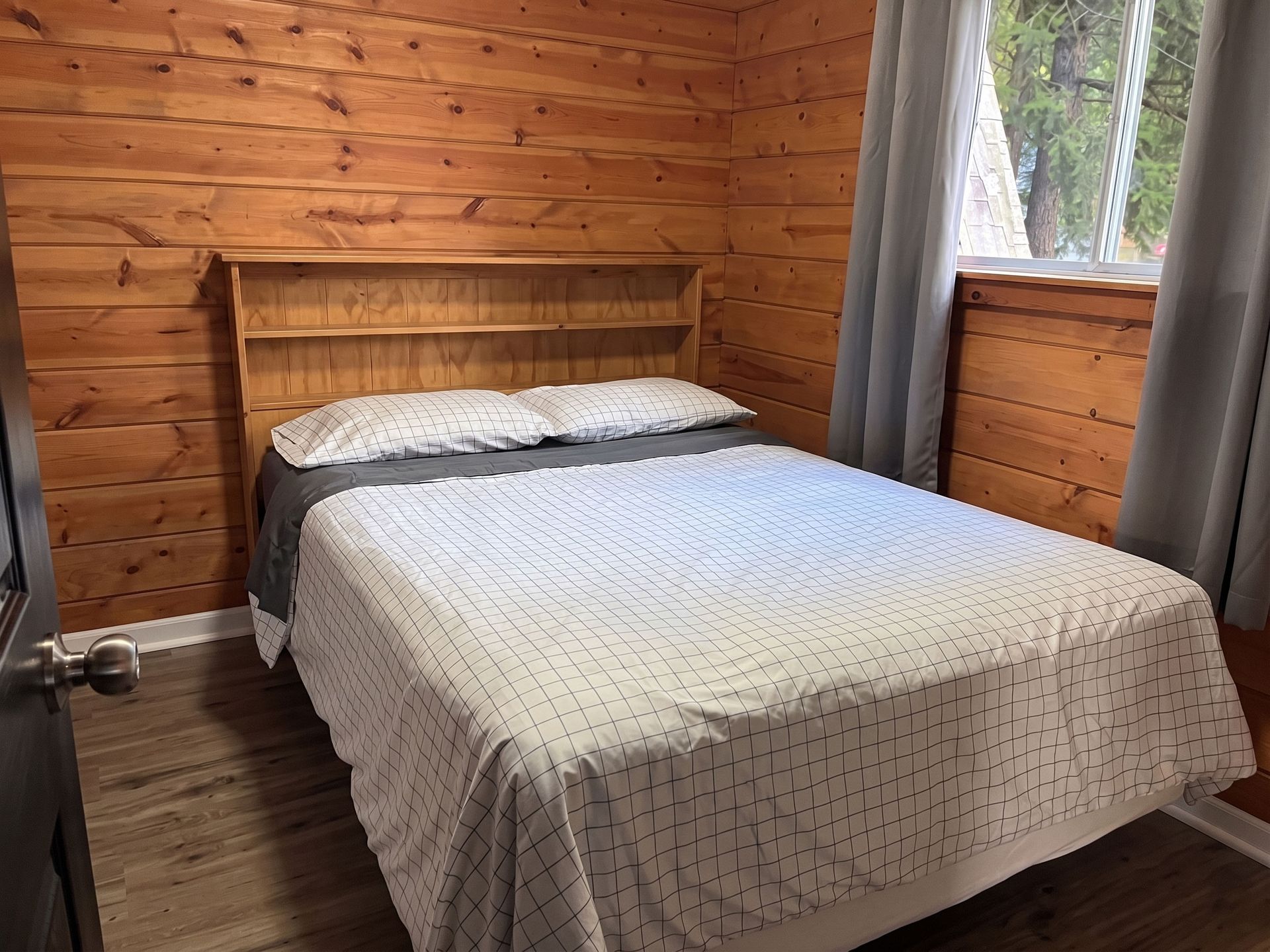 Cozy bedroom with a wooden wall, double bed, gray curtains, and window view of trees
