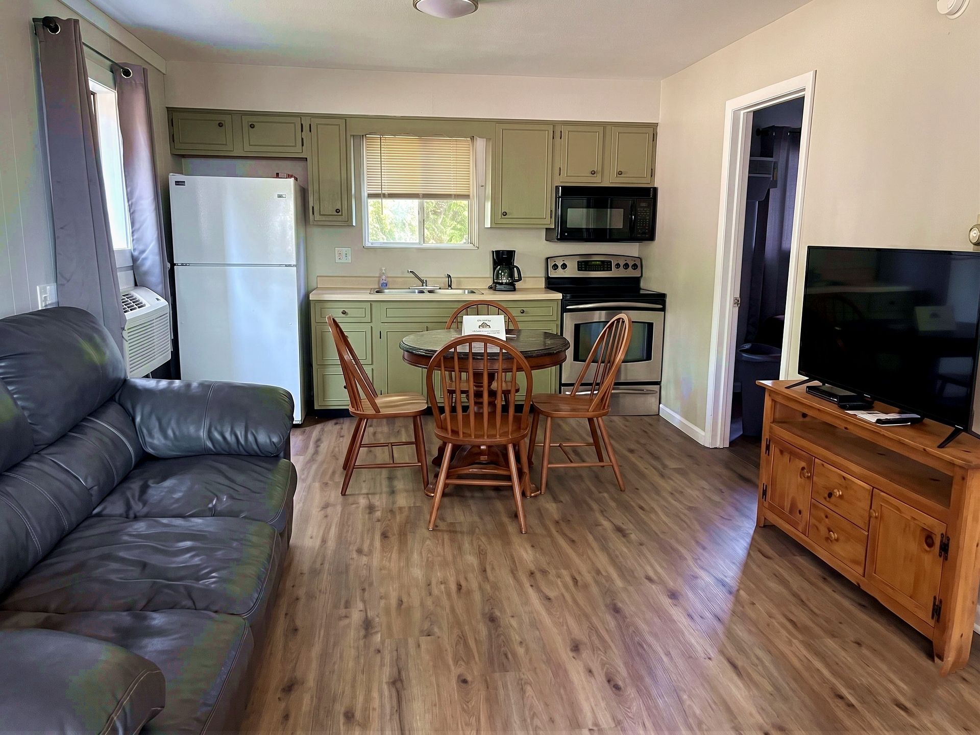 Living room with open kitchen, black couch, wooden table, and TV on a stand