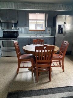 Dining area with round table and four wooden chairs in a kitchen with blue cabinets and stainless appliances.