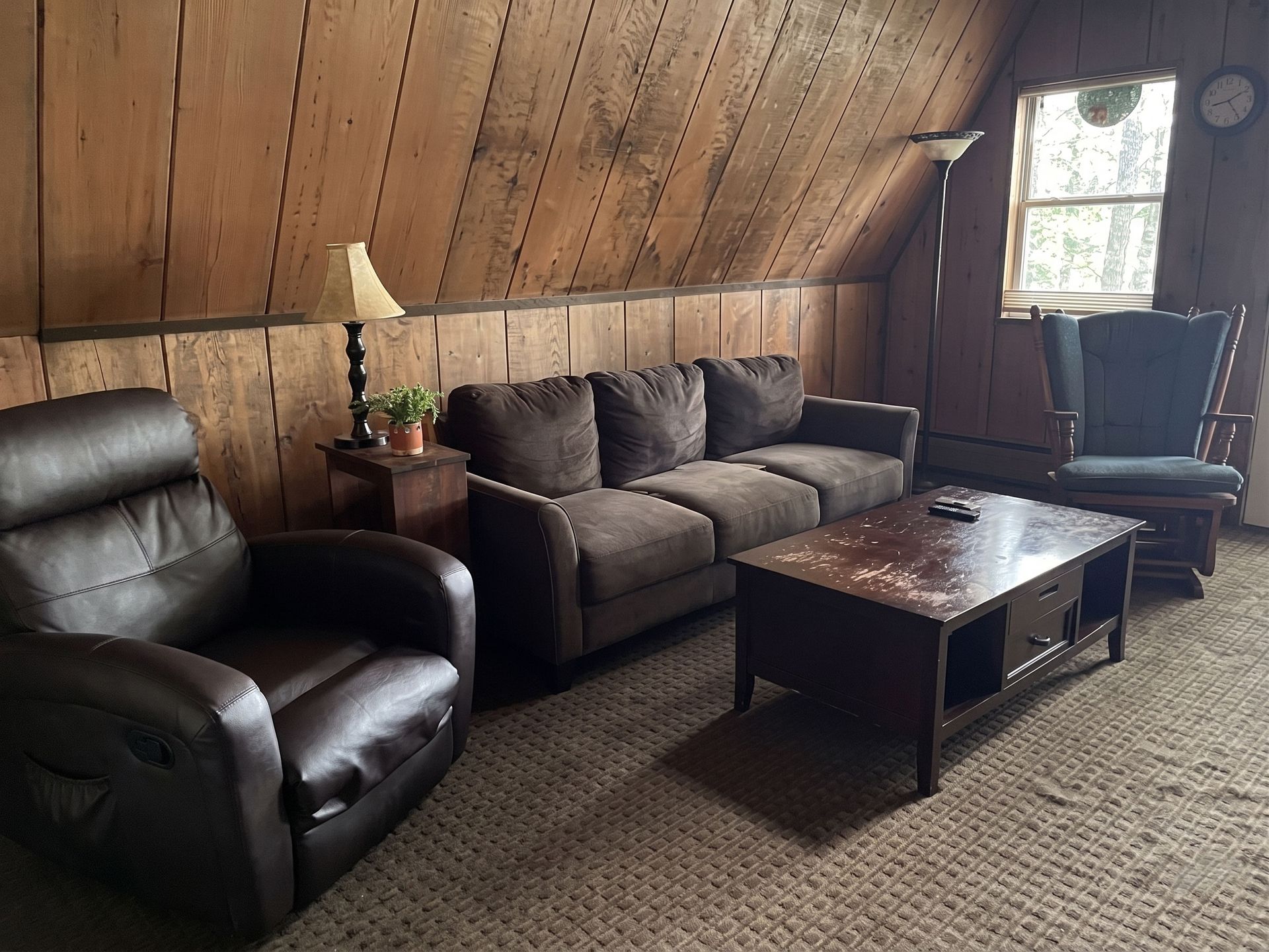 Cozy wood-paneled living room with leather chairs, gray sofa, coffee table, and window light