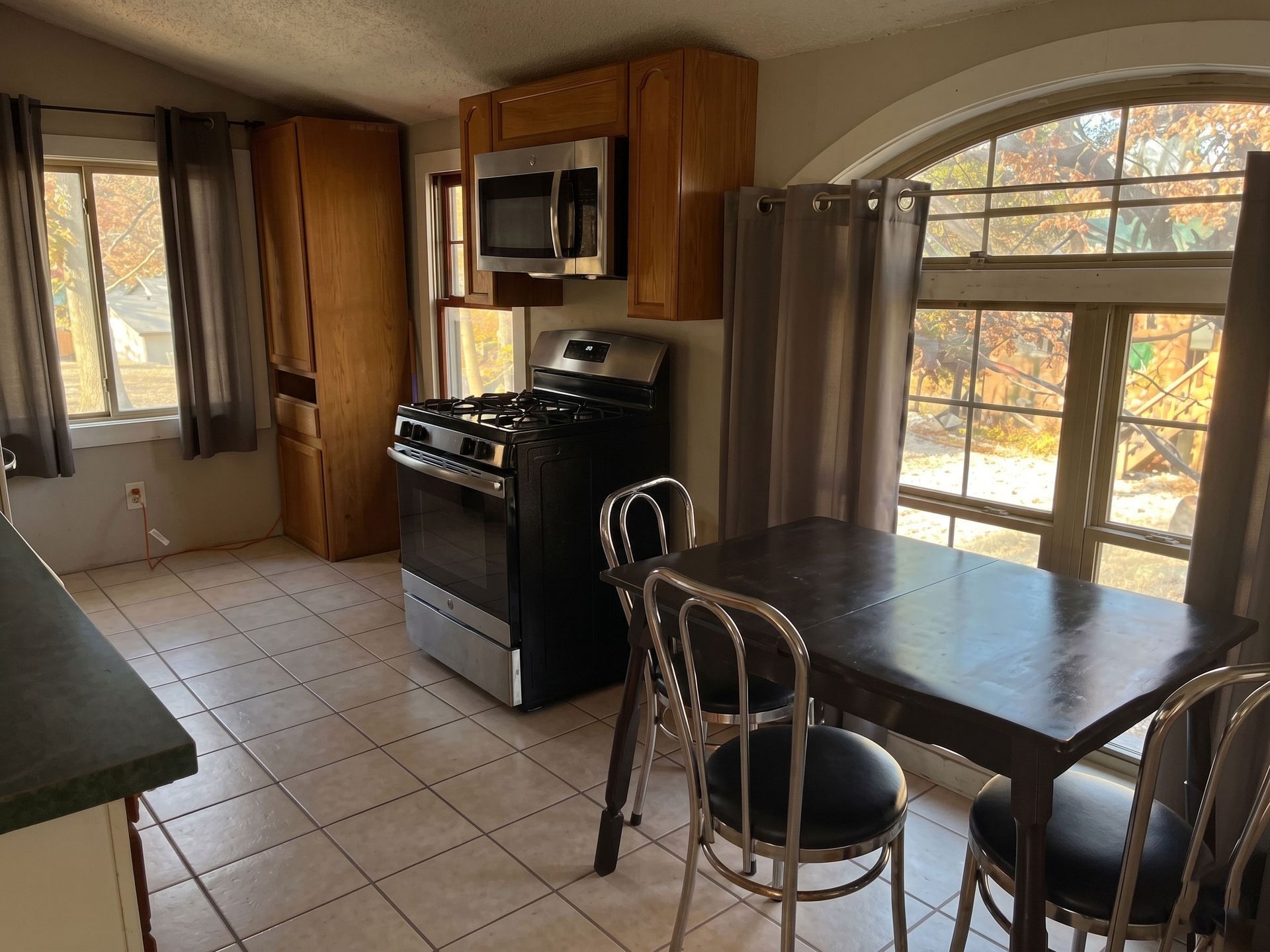 Small kitchen with stainless steel appliances, tile floor, and a dark wooden table by a window.
