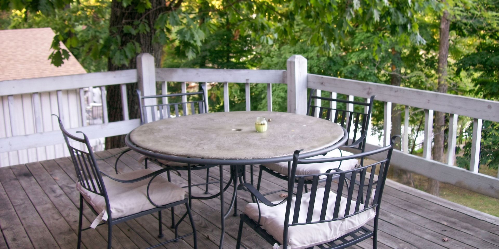 Patio table and chairs on a wooden deck with a white railing and trees in the background