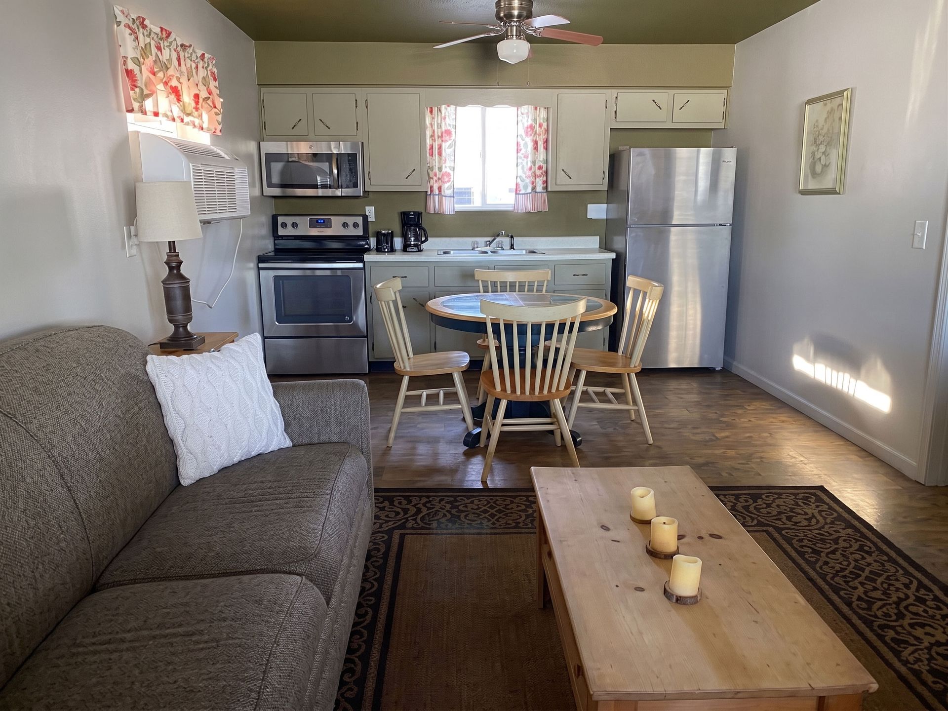 Small kitchen and dining area with gray sofa, wooden table, and stainless steel fridge.