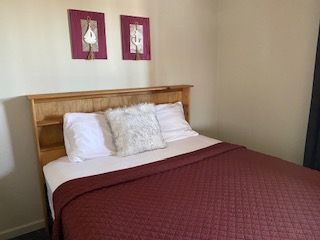Bedroom with a wooden bed, white pillows, burgundy quilt, and two framed wall prints above the headboard