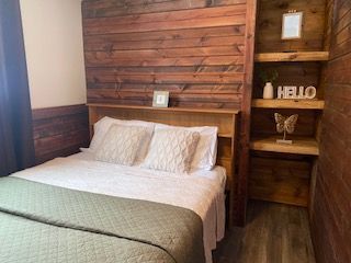 Cozy bedroom with a white bed, green throw, and rustic wooden wall and shelves