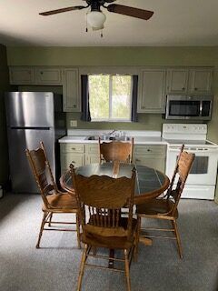 Kitchen with stainless fridge, white cabinets, stove, and round dining table with four wooden chairs
