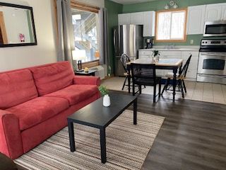Open-plan living room and kitchen with red sofa, black coffee table, dining set, and stainless steel appliances