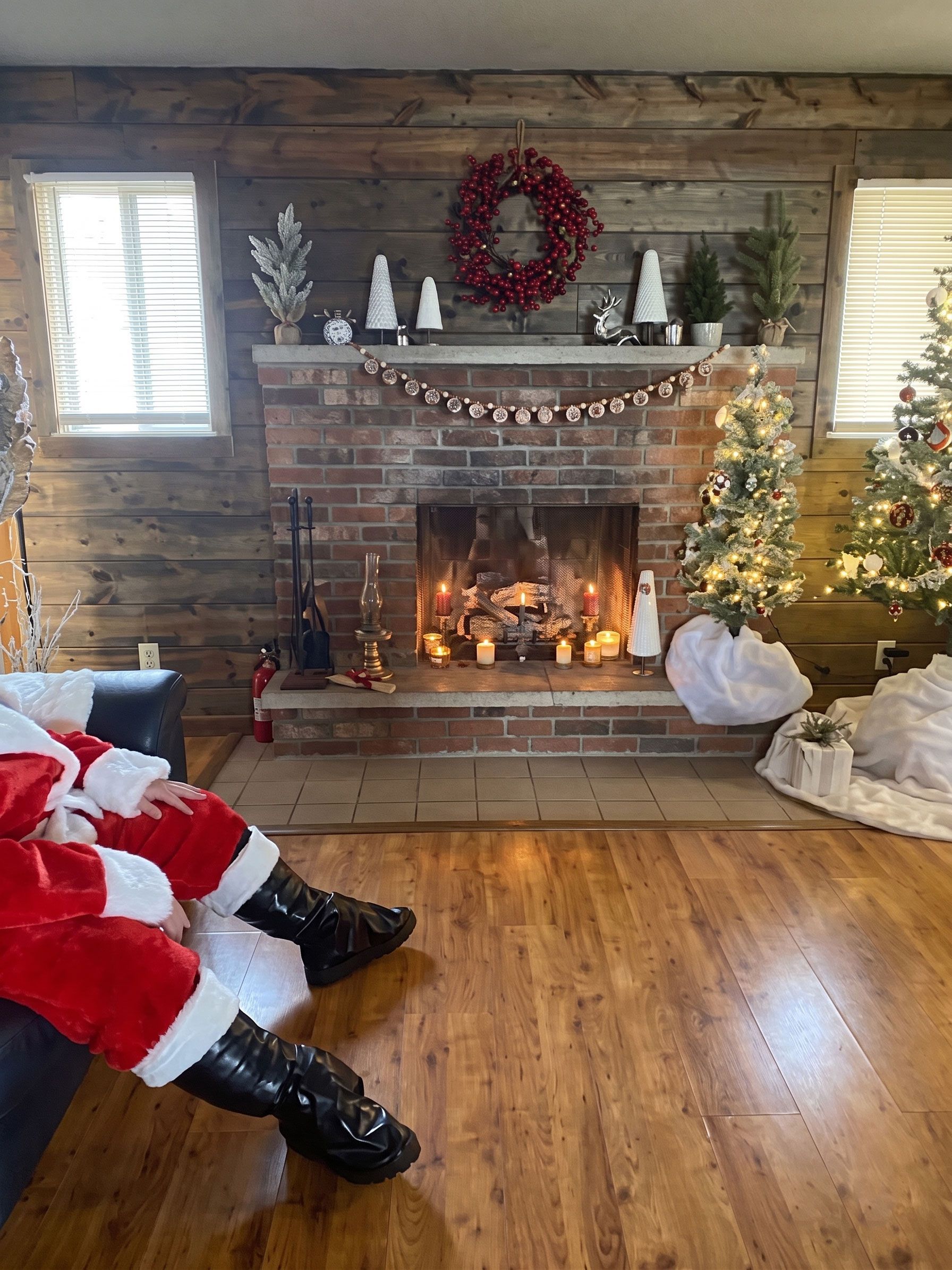 Santa seated by a fireplace in a cozy living room with a decorated Christmas tree and stockings on the mantel
