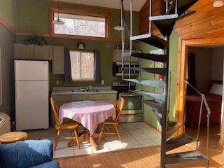 Small kitchen with spiral staircase, table, chairs, and refrigerator in a rustic wooden cabin.