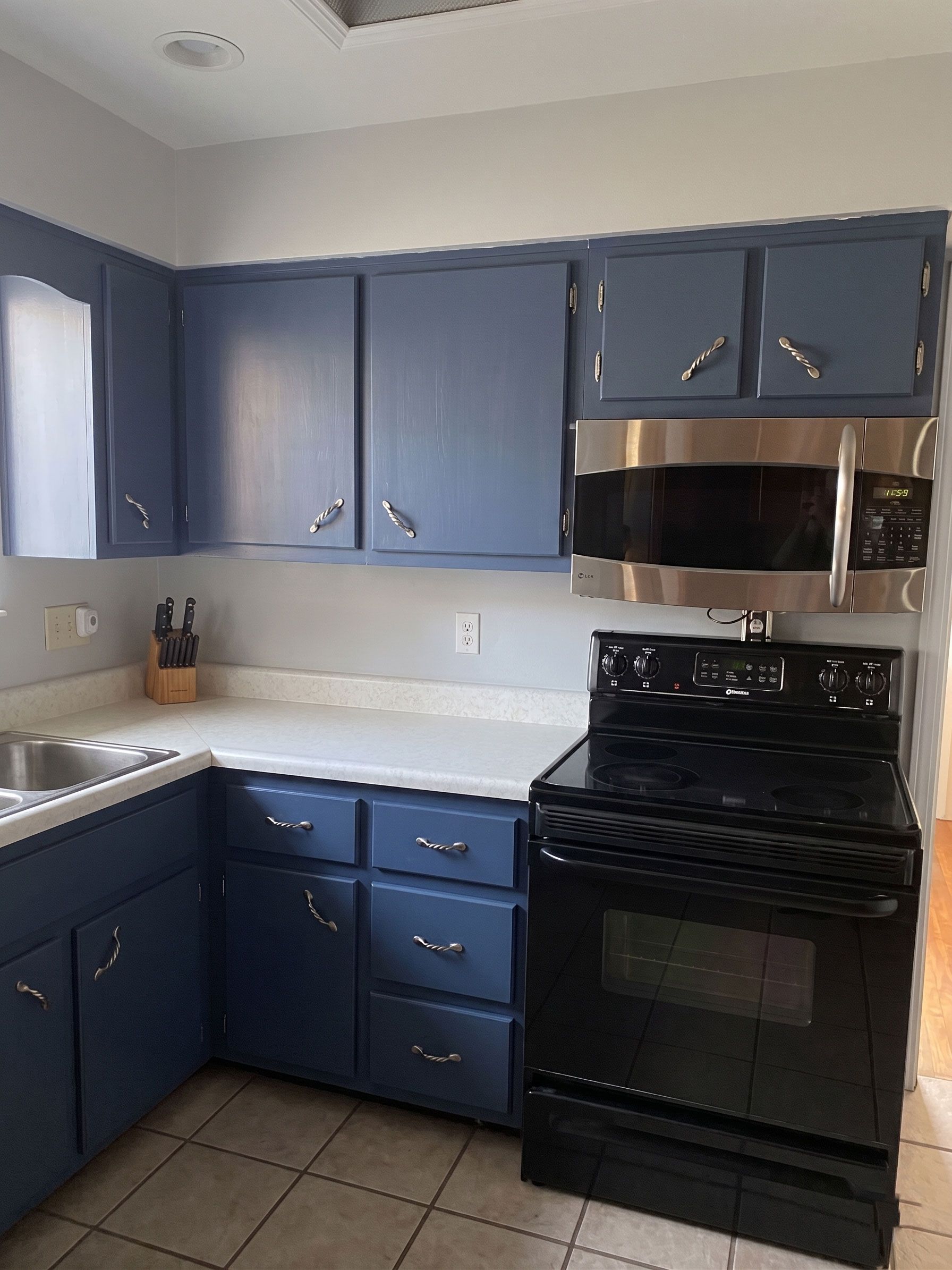 Small kitchen with blue cabinets, white countertops, and a black stove and microwave.