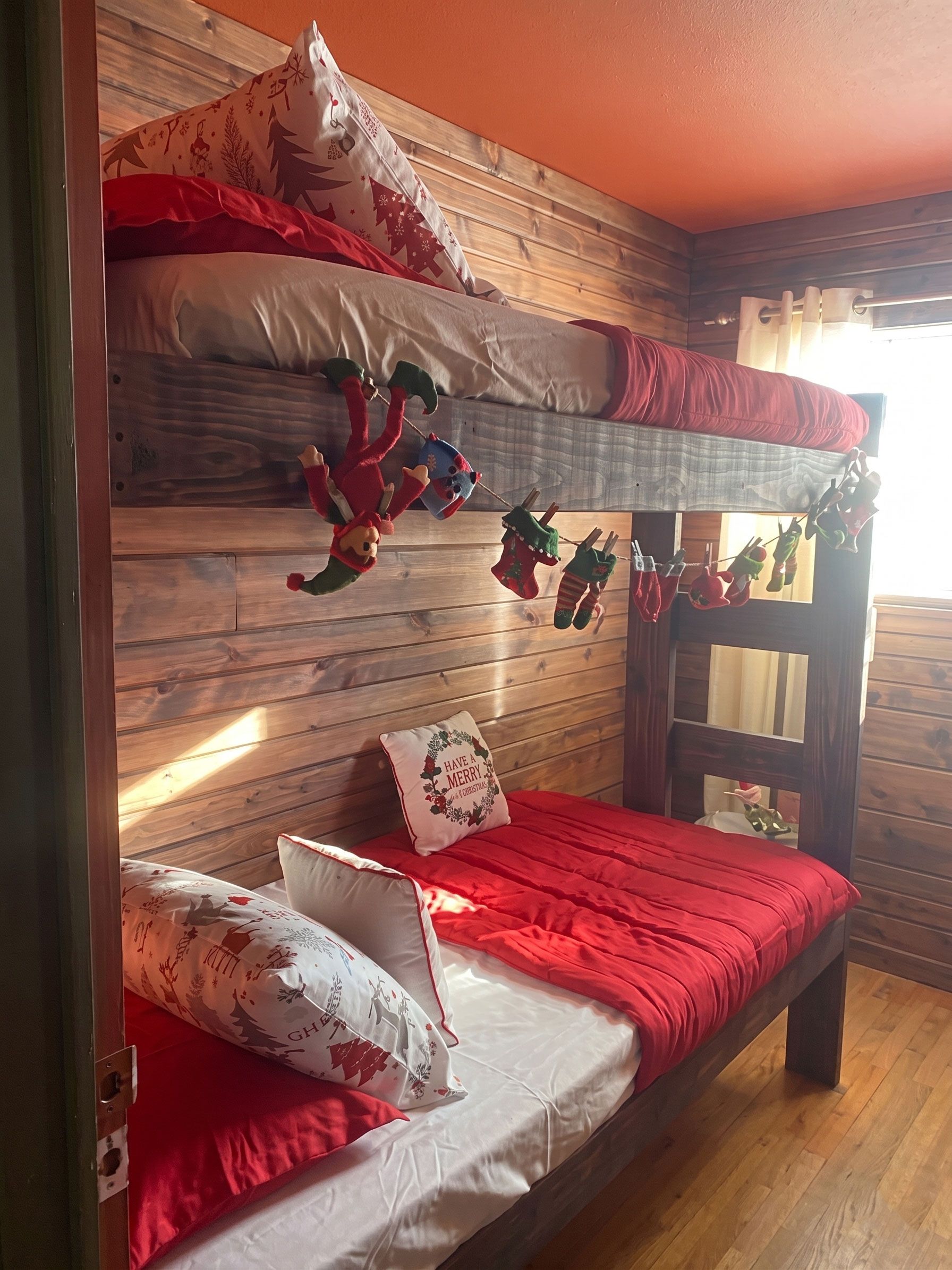 Wooden bunk bed with red bedding, holiday garlands, and a teddy bear in a cozy room