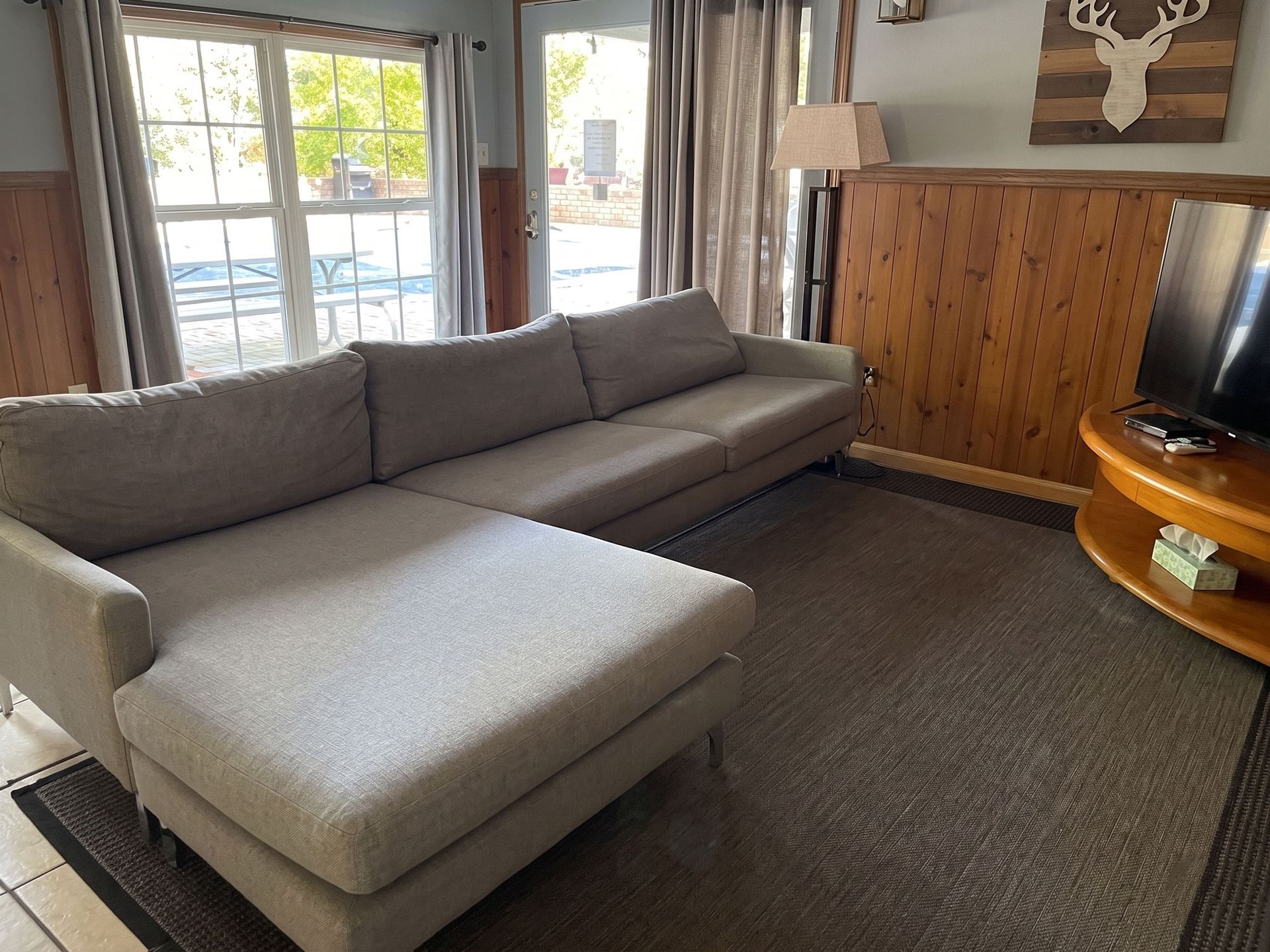 Gray sectional sofa with chaise in a cozy living room near windows and wood-paneled wall.