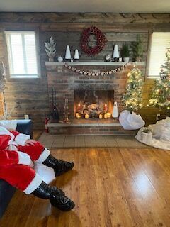 Cozy living room with lit fireplace, Christmas tree, garland, and Santa-suited legs by the hearth