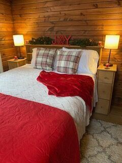 Red-and-white bed with plaid pillows, red throw, and warm bedside lamps against a wood-paneled wall.
