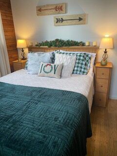 Cozy bedroom with teal quilt, plaid pillows, lamps on nightstands, and wall art above the bed