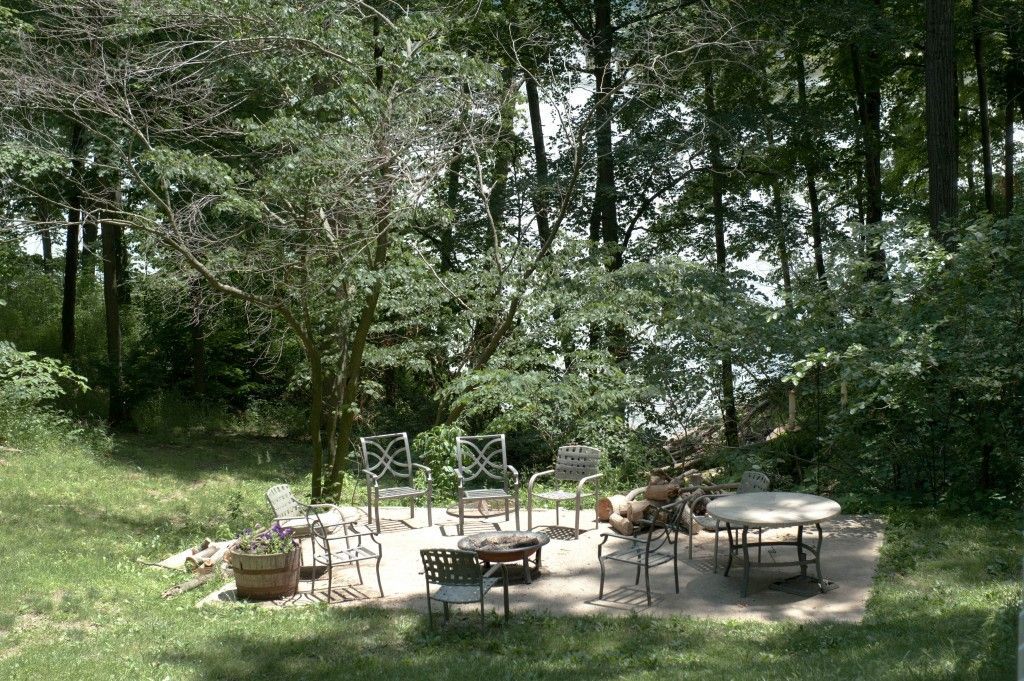Outdoor patio with tables and chairs in a shaded garden clearing surrounded by trees
