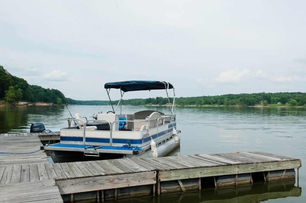 Pontoon boat docked beside a wooden pier on a calm lake under a cloudy sky
