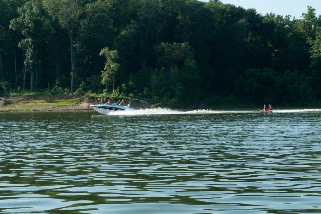 Speedboat skimming across a lake, leaving a white wake near a forested shore