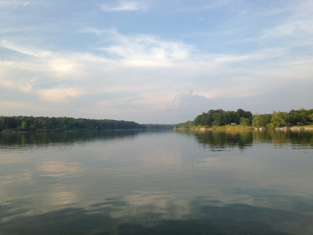 Calm river reflecting a cloudy sky, with tree-lined shores on both sides.